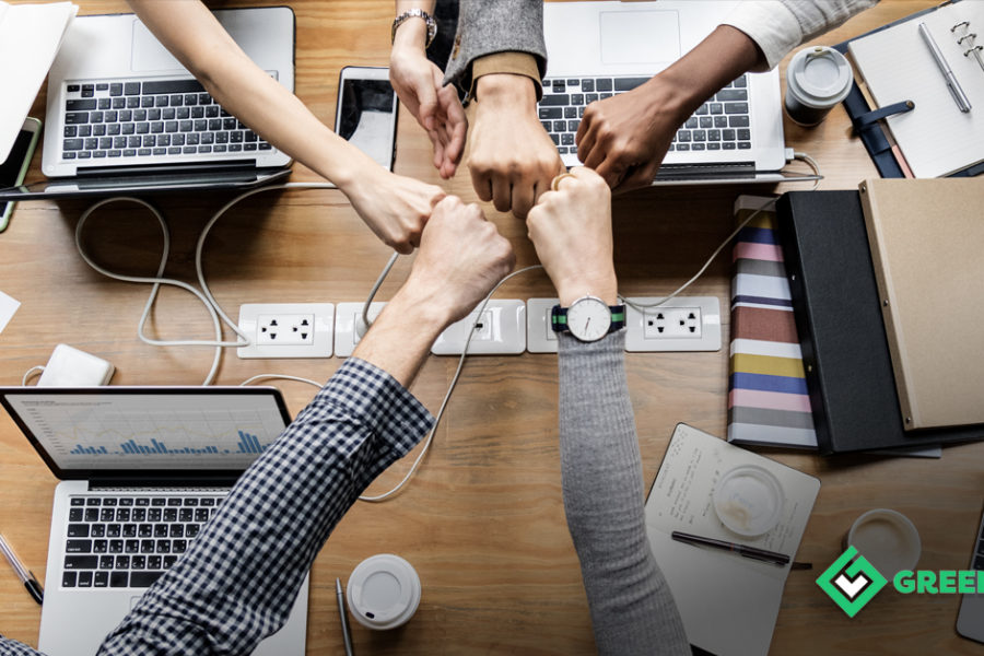NewBossCommunications. A birds eye photo of a desk with 5 people fistbumping over laptops.